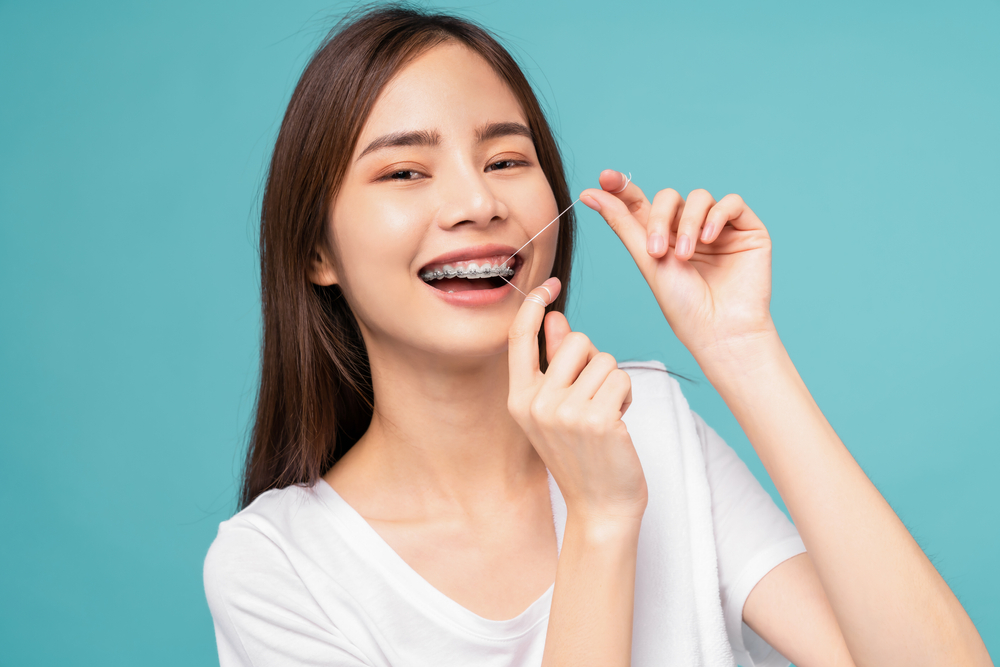 Young,Asian,Woman,Cleaning,Braces,On,Teeth,With,Dental,Floss